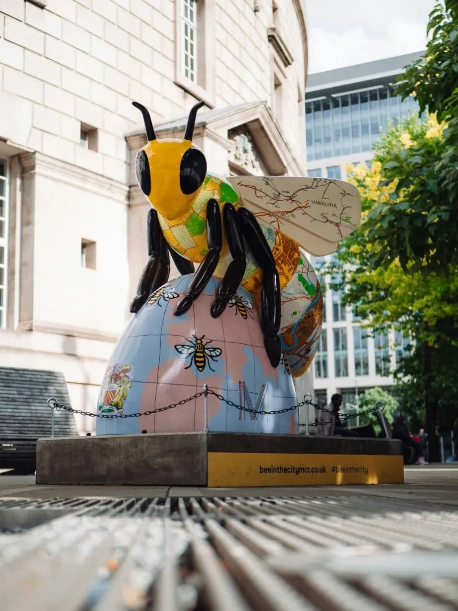 A sculpture of a Manchester bee sat on top of an egg shaped globe with bees drawn on the globe.
